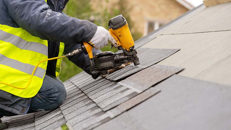 Roofer in Special Protective Work Wear Installing New Shingles in Home Roof